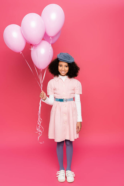 full length view of african american girl in trendy spring outfit posing with festive balloons on pink - 写真・画像