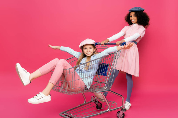 афроамериканська дівчина поблизу збудженого друга, що їде на шопінгу на рожевому візку
 - Фото, зображення