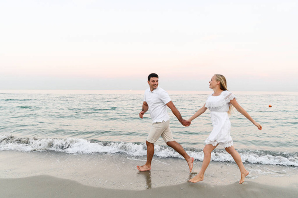 Парень в летней одежде ходит по океану. муж и жена на романтическом закате дня у моря. любовники бегают по пляжу. Медовый месяц для молодоженов. - Фото, изображение