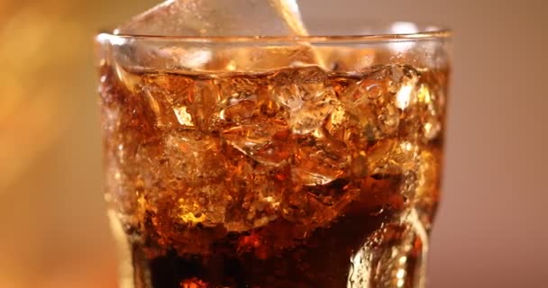 Glas Cola met ijsblokjes van dichtbij. Cola drinken met ijs en bellen in glas close-up. Draaiend glas Cola drinken over wazige achtergrond. Langzame beweging draaien 4K video-opnames - Video