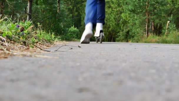 Una chica en un scooter va a la distancia. Un niño en chándal. Verano en el bosque. 4k. HD - Metraje, vídeo