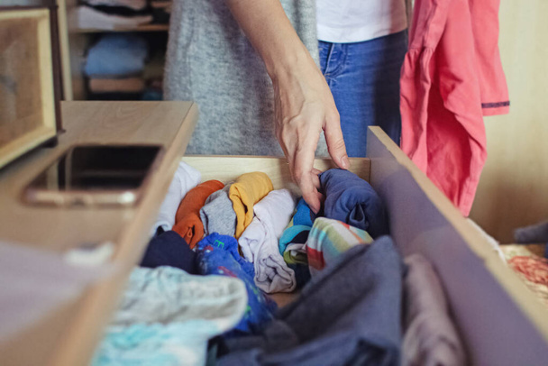 A woman is sorting through things in her home wardrobe with her hands. Folding clothes after washing. Household responsibilities, keeping the apartment clean and tidy - Photo, Image
