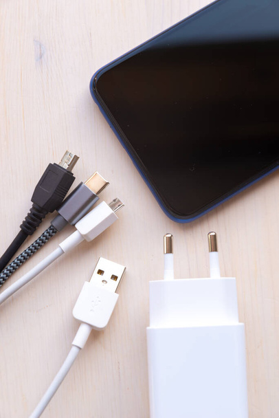 Okostelefon, USB töltő, mikroUSB kábelek és csatlakozók, mini USB, c típusú USB, fa felületen. USB töltőcsatlakozók. - Fotó, kép
