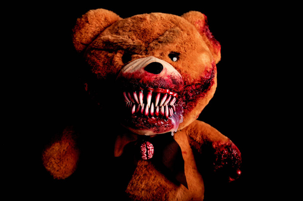 oso aterrador con una sonrisa sangrienta espeluznante sobre un fondo negro. juguete de terror. concepto de Halloween. una pata cortada y una oreja mordida cubierta de sangre - Foto, Imagen