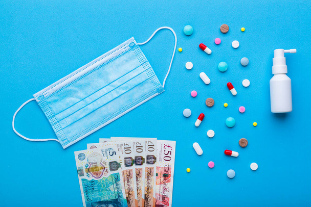A lot of pills on a blue background with pounds cash banknotes as a symbol of health insurance on pandemic time. - Photo, Image