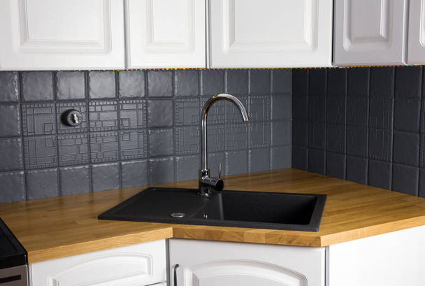 Nahaufnahme der neuen modernen Küche Massivholz Eiche Zähler mit eingebauten schwarzen rechteckigen Granit-Spüle, neu gestrichen grauer Farbe Fliesenwand. Eckschrank. - Foto, Bild