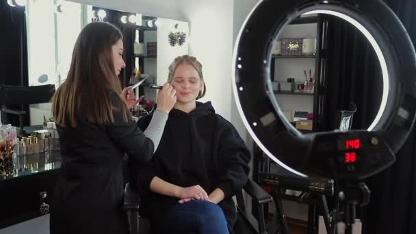 Woman make makeup for attractive blond hair woman in studio. Selective focus of digital camera with makeup artist applying cosmetics for beautiful model. Ring lamp - Footage, Video