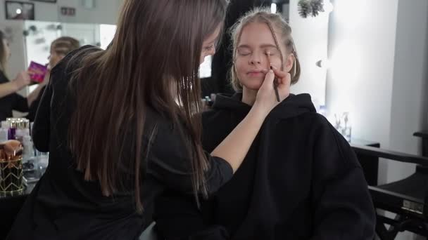 Woman make makeup for attractive blond hair woman in studio. Video of makeup artist applying cosmetics for beautiful model - Footage, Video
