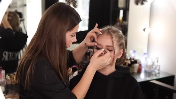 Kobieta zrobić makijaż dla atrakcyjnej blond włosy kobieta w studio. Wideo z makijażystą stosującym kosmetyki dla pięknej modelki - Materiał filmowy, wideo