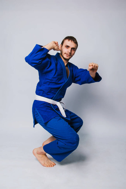 Jongeman in een blauwe kimono op een witte achtergrond. Hij is een beginner in vechtsport. studiofoto - Foto, afbeelding