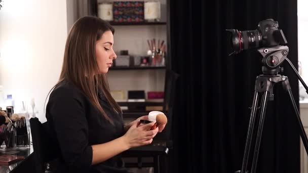 Young beautiful woman and professional beauty make up artist vlogger recording makeup tutorial in beuty studio to share on website or social media. Blogger use digital camera on tripod and ring lamp - Footage, Video