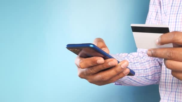 Мужчина держит в руках кредитную карту и пользуется смартфоном для покупок онлайн - Кадры, видео