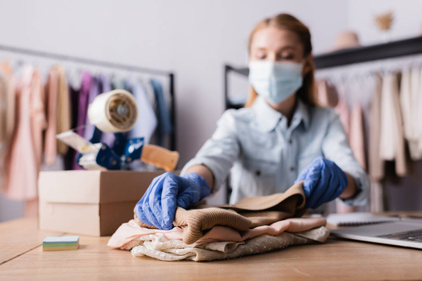 showroom proprietor in medical mask, working with clothes at workplace on blurred background - Photo, Image