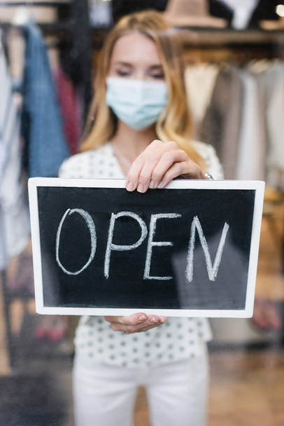 majitel lékařské masky s otevřeným nápisem v módním butiku, rozmazané pozadí - Fotografie, Obrázek