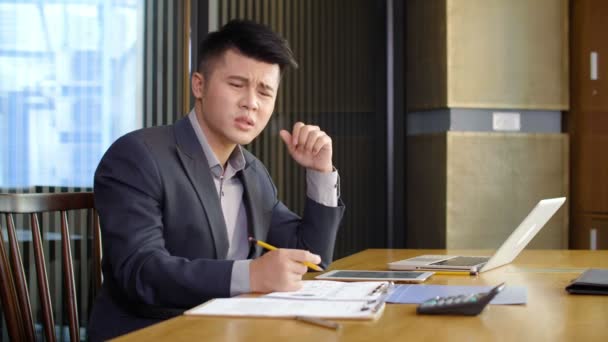 Blocco di uomo d'affari asiatico con faccia da cad seduto alla scrivania, guardando attraverso i grafici e calcolando i numeri sulla calcolatrice - Filmati, video