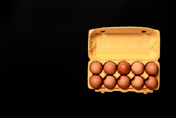 Naturalne organiczne jaja kurze w żółtym opakowaniu kartonowym izolowane na czarnym tle, widok z góry, z miejsca na ksero, puste miejsce tekstowe. Wizytówka sklepu spożywczego. Świeże jedzenie na farmie. Zdrowe odżywianie. Dziesięć. - Zdjęcie, obraz