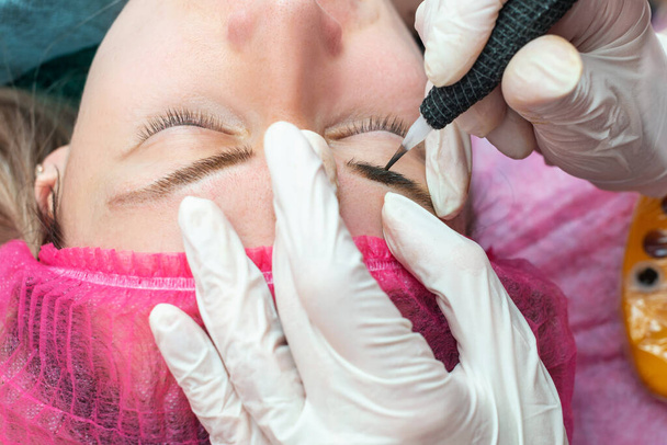 Hands makes permanent makeup eyebrow procedure applying pigment.  - Photo, Image