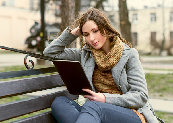 νεαρή γυναίκα κάθεται με δισκίο και ανάγνωση - Φωτογραφία, εικόνα