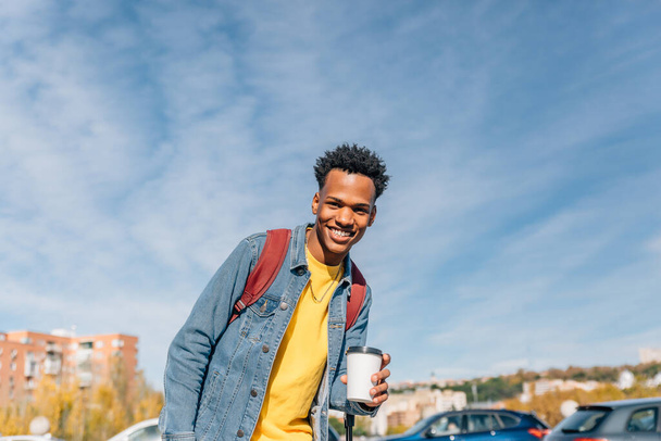 Attraktiver schwarzer Mann in Jeansjacke trinkt Kaffee auf der Straße einer Stadt - Foto, Bild