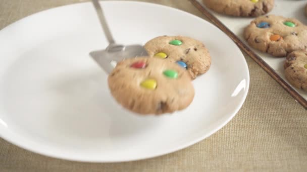 Cookies με πολύχρωμα M & Ms καραμέλες τοποθετούνται σε ένα λευκό άδειο πιάτο - Πλάνα, βίντεο