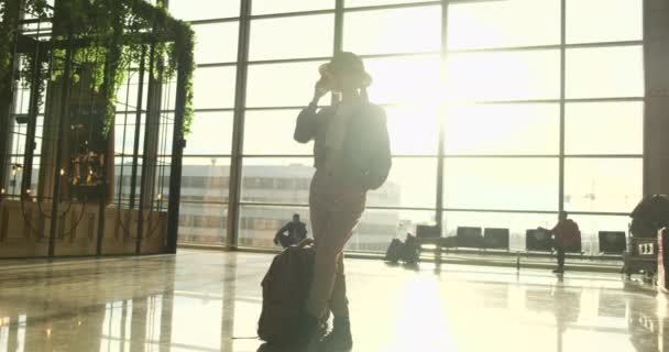 Jovem de pé com telefone perto da janela do aeroporto à espera do voo - Filmagem, Vídeo