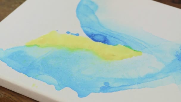 Arte Fluida. Pintura azul e amarela abstrata. Close up de artista feminina usa spray de água para misturar tintas amarelas e azuis - Filmagem, Vídeo