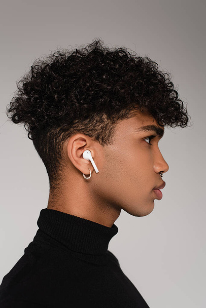 vista laterale dell'uomo afroamericano che ascolta musica in auricolari senza fili isolati su grigio - Foto, immagini