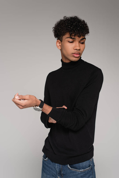 young african american man adjusting sleeve on turtleneck sweater isolated on grey - Foto, Imagem