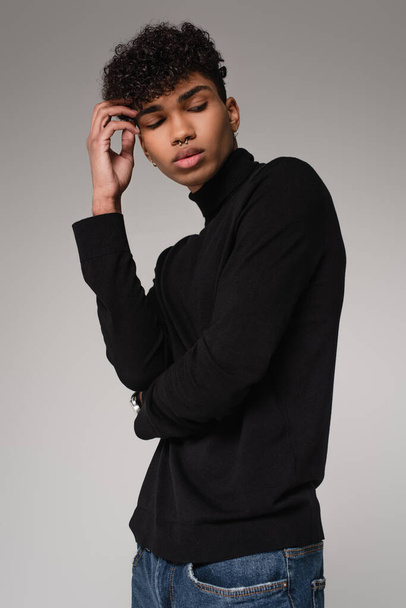 молодий афроамериканський чоловік в чорному жахливому светрі позує ізольовано на сірому
 - Фото, зображення