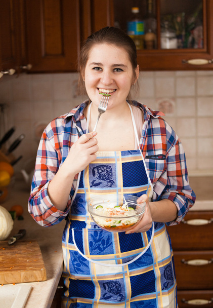 Sourire femme au foyer manger de la salade sur la cuisine
 - Photo, image