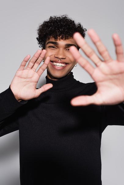 curly african american man in black turtleneck sweater smiling while showing stop gesture isolated on grey - Photo, Image