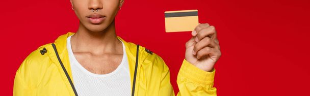 partial view of african american man in jacket holding credit card isolated on red, banner - Photo, Image