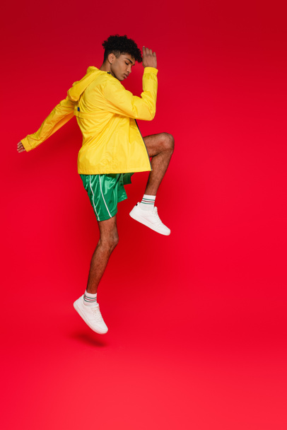 longitud completa del hombre afroamericano deportivo en chaqueta amarilla trabajando en rojo - Foto, Imagen