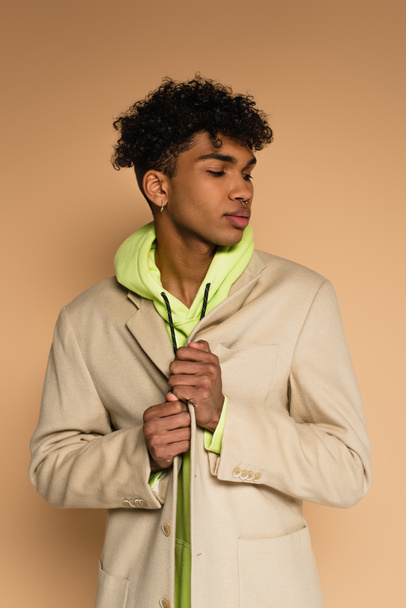 hombre afroamericano de moda en sudadera con capucha y chaqueta posando en beige - Foto, imagen