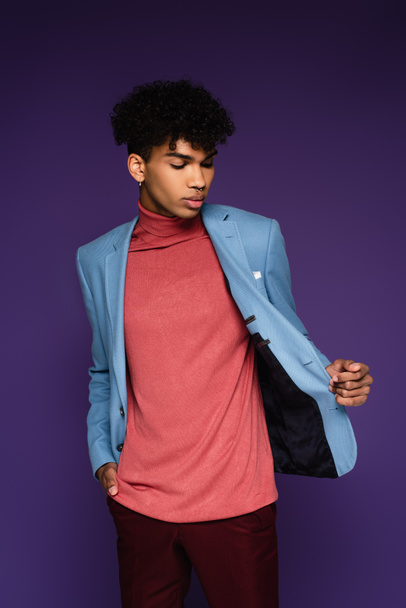 młody Afroamerykanin człowiek dostosowując niebieski blezer patrząc daleko na fioletowy - Zdjęcie, obraz