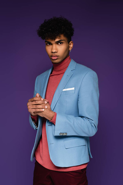 young african american man in stylish blazer looking at camera on purple - 写真・画像