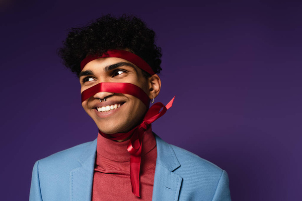 pozitivní africký Američan svázaný červenou stuhou na fialové  - Fotografie, Obrázek