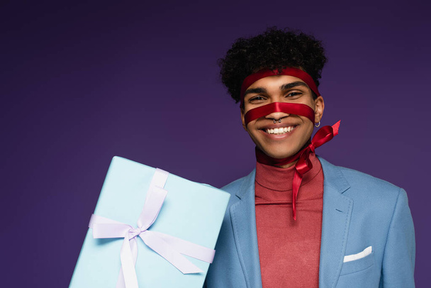 joyful african american man tied with ribbon near present on purple  - Photo, Image