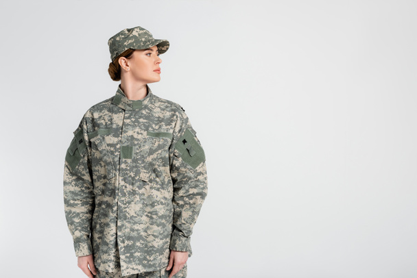 Στρατιώτης με καπέλο και στολή κοιτάζει μακριά απομονωμένος στο γκρι  - Φωτογραφία, εικόνα