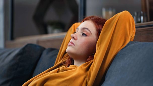 Teenager looking away while sitting on couch in living room  - Photo, Image