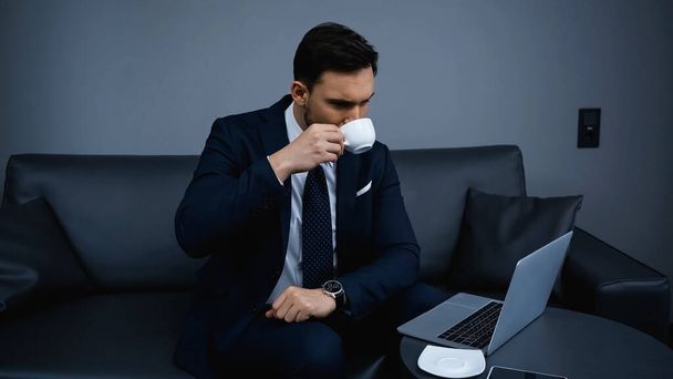 Businessman drinking coffee near laptop and smartphone in hotel room  - 写真・画像