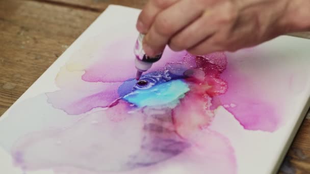 Vista dall'alto dell'uomo artista dipinge un quadro astratto, versa una vernice rosa dal tubo su tela bagnata - Filmati, video