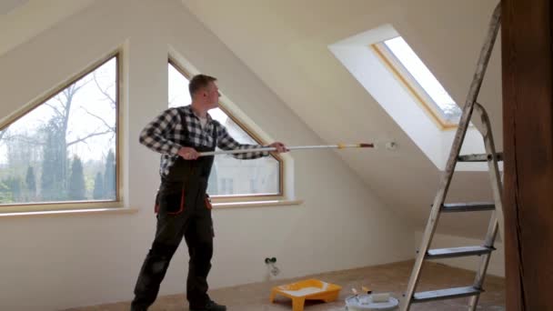 Heimwerkerkonzept, Handwerker streichen eine Wand mit weißer Farbe in der Nähe des Dachfensters im Dachgeschoss - Filmmaterial, Video