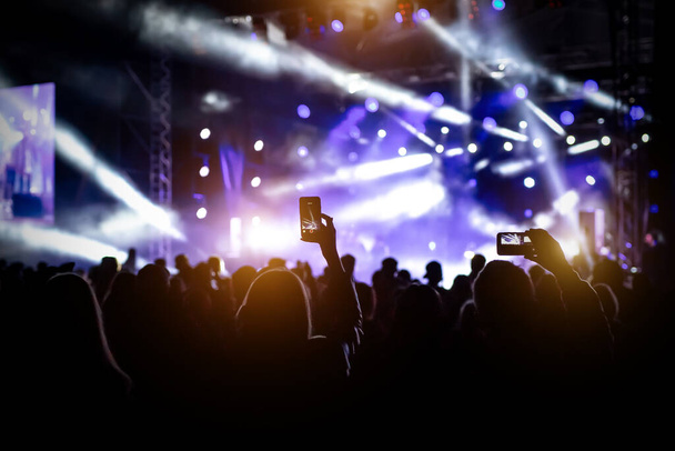 Pessoas com mãos levantadas, silhuetas de multidão de concertos na frente de luzes de palco brilhantes - Foto, Imagem