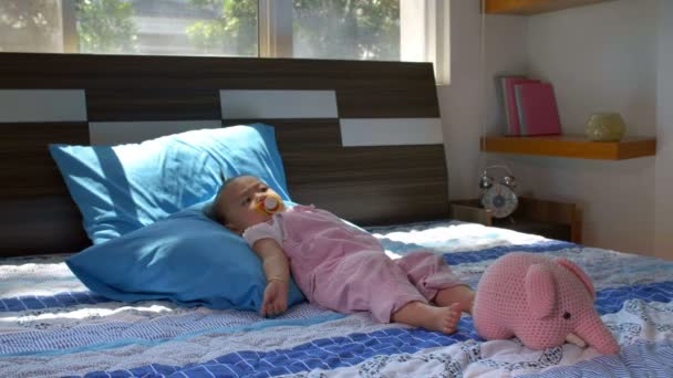 Szerokie ujęcie dziewczynki z sutkiem w ustach leżącej na dużym łóżku - Materiał filmowy, wideo