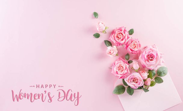 Szczęśliwego Dnia Kobiet. Widok z góry kwiat róż i "Szczęśliwego Dnia Kobiet" tekst na różowym pastelowym tle. - Zdjęcie, obraz