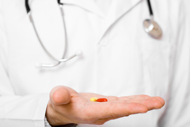 Doctor aislado sobre fondo gris ofreciendo píldora en su palma
 - Foto, Imagen