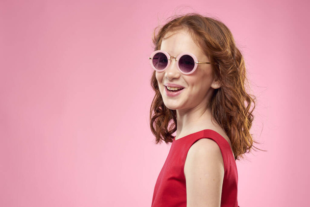 Mädchen mit lockigem Haar Sonnenbrille Kindheit Freude rosa Hintergrund - Foto, Bild