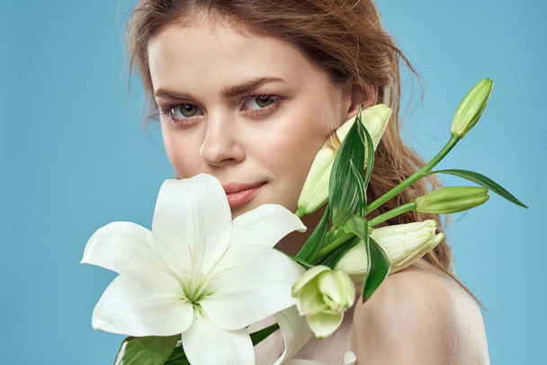 Mujer con un ramo de flores blancas sobre un fondo azul hombros desnudos hermosa cara - Foto, imagen