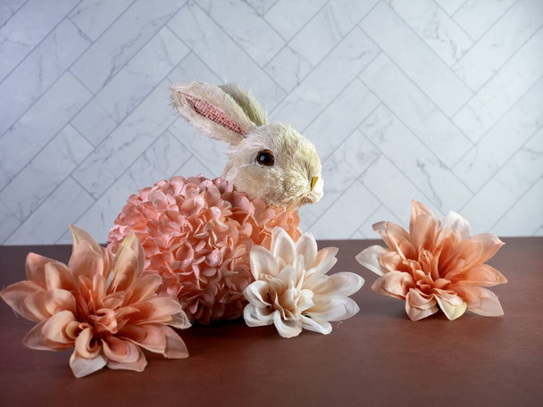 春とイースターの家の装飾のために桃のダリアの花が咲くとヘリンボーンタイルの壁とテラコッタのカウンターに座って桃の花で覆われたイースターウサギのバニー詰め. - 写真・画像